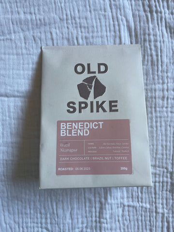 A single pack of ground Old Spike Coffee in sustainable paper cream packaging, on a white muslin fabric background.