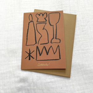 Photo of a burnt orange card and gold envelop laid on a white cotton muslin fabric. The card has minimalist abstract shapes on it with gold embossed writing that says 'Celebrate'.