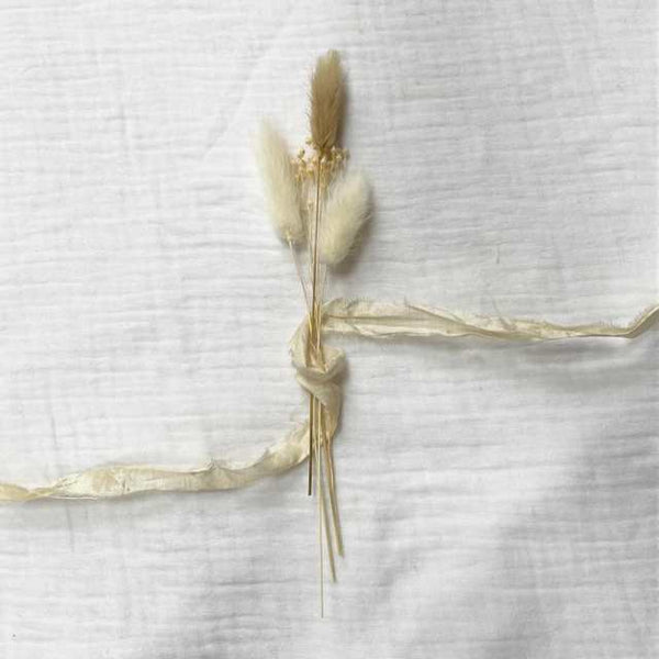 Photo of a small bouquet of natural dried flowers laid on a white muslin fabric background. It’s wrapped and encompassed by recycled sari silk Centred.