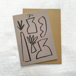 Photo of a purple card and gold envelop laid on a white cotton muslin fabric. The card has minimalist abstract shapes on it.