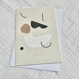 Photo of a cream card and white envelop laid on a white cotton muslin fabric. The card has minimalist abstract shapes on it with gold embossed writing that says 'new one'.